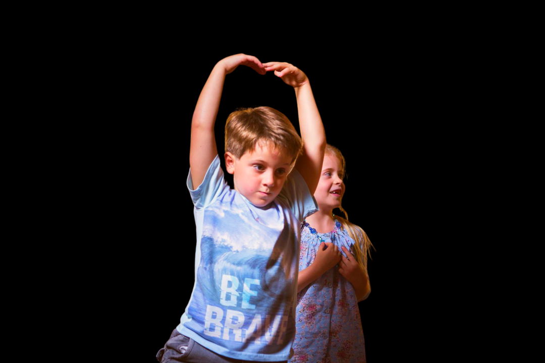 Young boy dancing in forefront with young girl smiling in the background. 