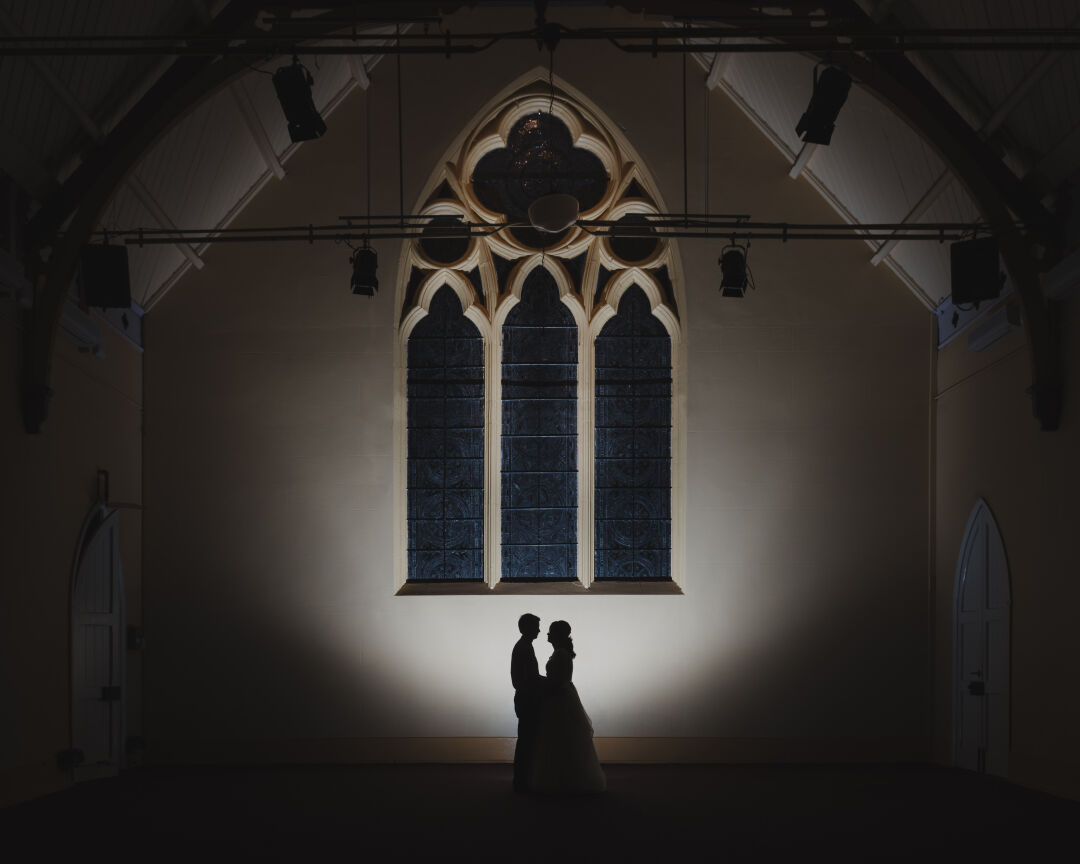 Wedding couple silhouetted against the stained glass window in the Church Theatre