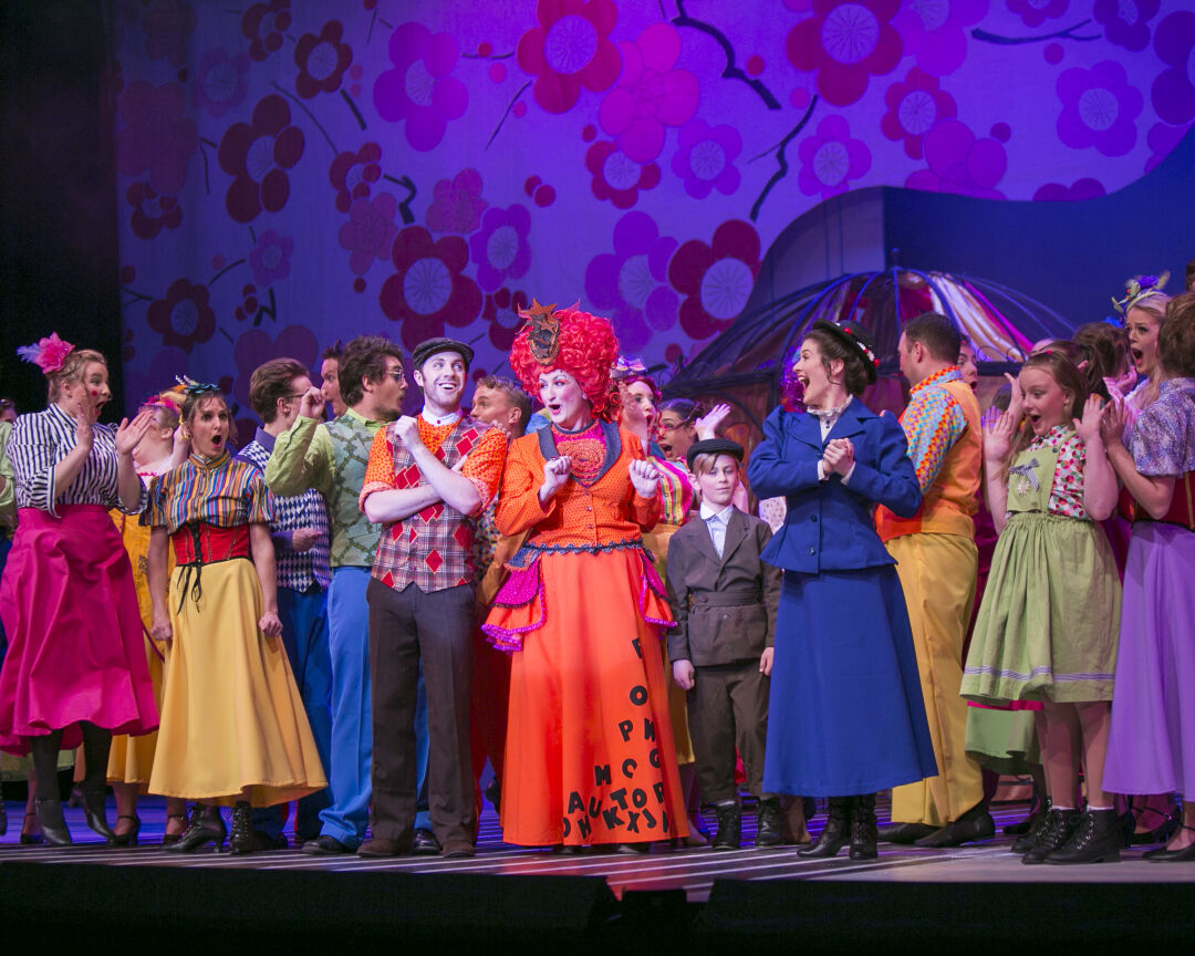 Large number of the cast performing and singing on stage.