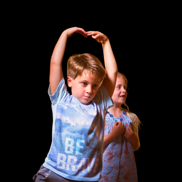 Young boy dancing in forefront with young girl smiling in the background. 