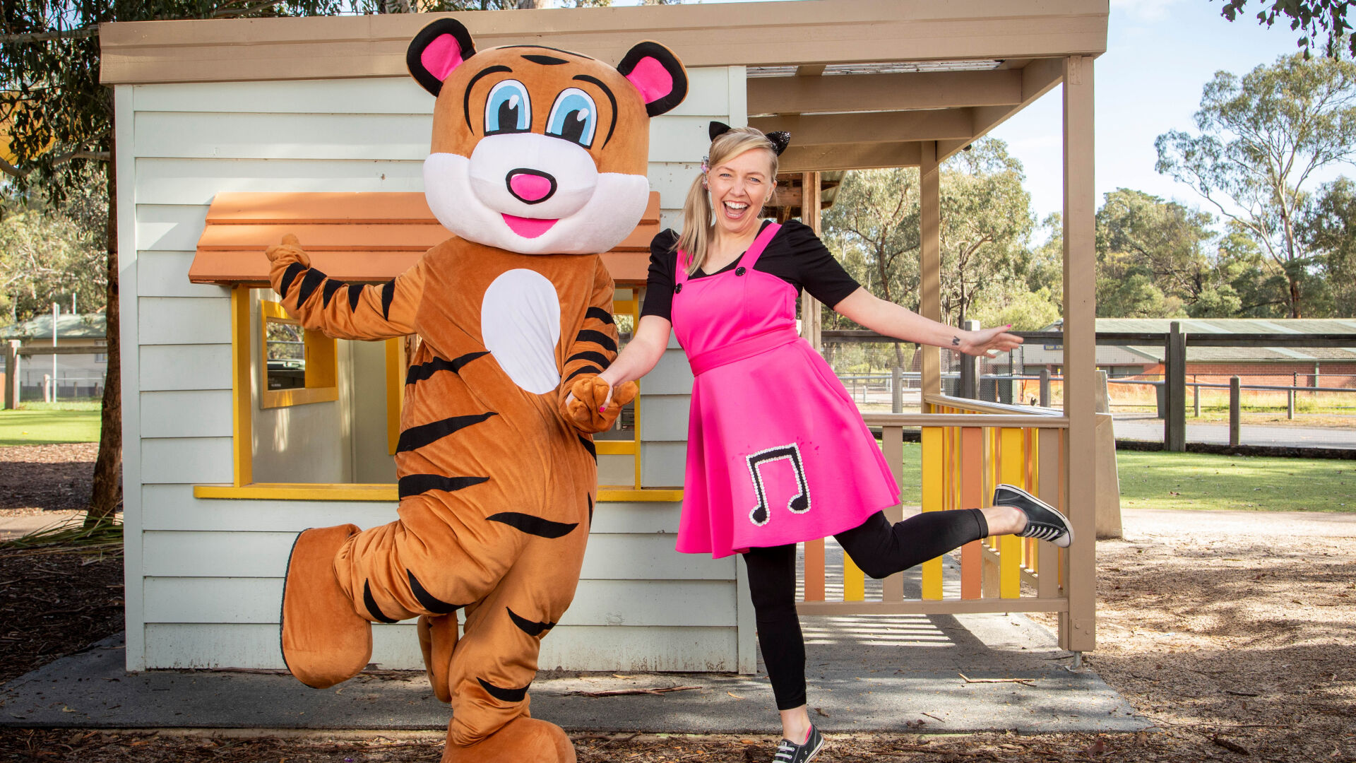 Sarah and Pevan the Tiger Mascot pose while holding hands and kicking one leg up with smiling faces